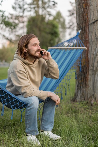 Vista lateral del hombre en hamaca hablando por teléfono inteligente