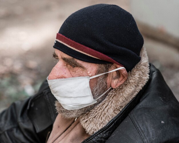 Vista lateral del hombre sin hogar al aire libre con máscara médica