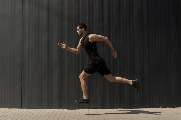 Vista lateral de un hombre joven y atlético en forma saltando y corriendo.