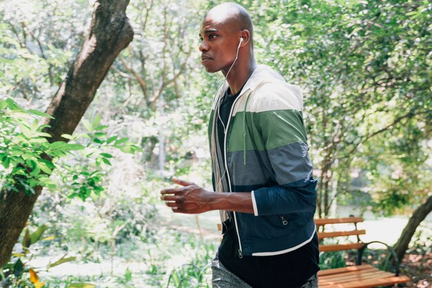 Vista lateral de un hombre joven con el auricular en su oreja corriendo en el parque