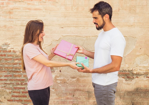 Vista lateral del hombre joven y la mujer dando regalo de San Valentín el uno al otro