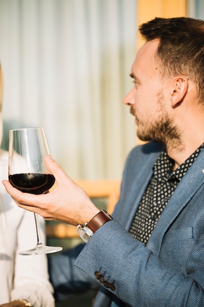 Foto gratuita vista lateral del hombre joven que sostiene el vidrio de vino rojo en su mano