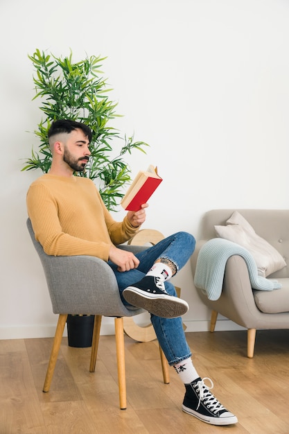 Foto gratuita vista lateral del hombre joven serio hermoso que se sienta en la silla que lee el libro