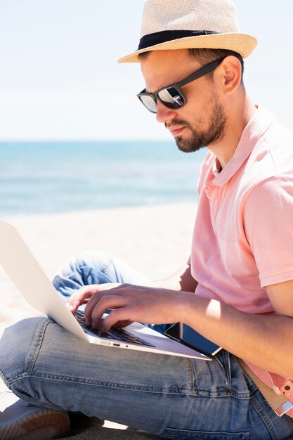 Vista lateral del hombre con laptop en la playa