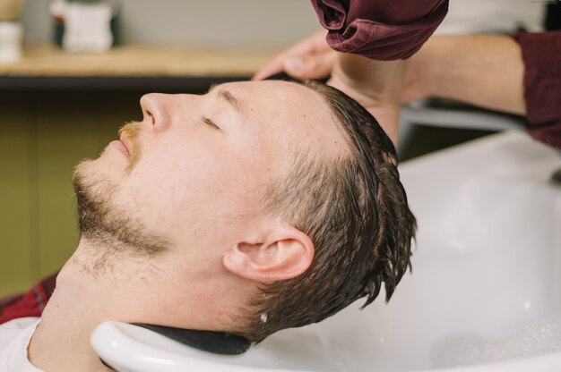 Vista lateral del hombre lavarse el cabello en la peluquería