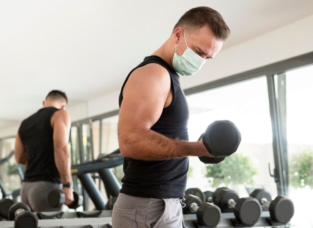 Vista lateral del hombre con máscara médica haciendo ejercicio en el gimnasio