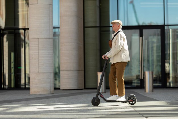 Vista lateral del hombre mayor en la ciudad montando un scooter eléctrico