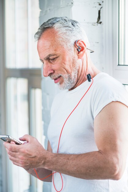 Vista lateral de un hombre mayor que disfruta de la música en el teléfono móvil a través del auricular