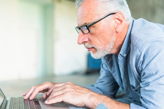 Vista lateral del hombre mayor que usa la computadora portátil