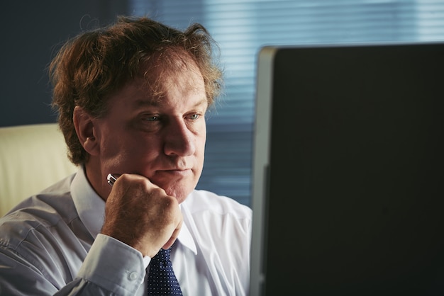 Vista lateral del hombre de mediana edad leyendo artículos de negocios en la red en el trabajo