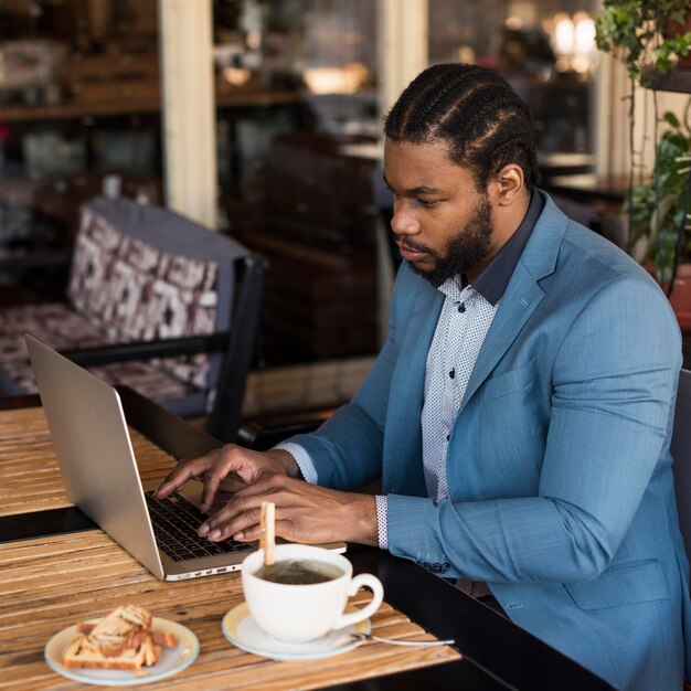 Vista lateral del hombre moderno trabajando en su computadora portátil en un restaurante
