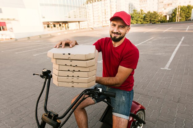 Vista lateral del hombre en motocicleta con cajas de pizza