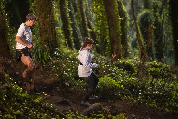 Vista lateral del hombre y la mujer activos caminando en el bosque por la noche. Dos deportistas con ropa deportiva pasando tiempo al aire libre. Ocio, naturaleza, concepto de hobby.