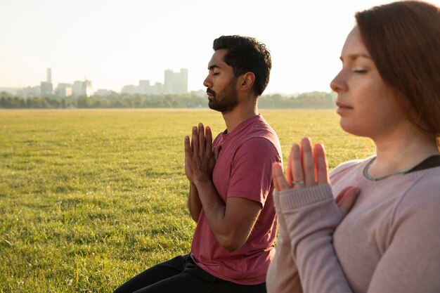 Vista lateral del hombre y la mujer meditando al aire libre con espacio de copia