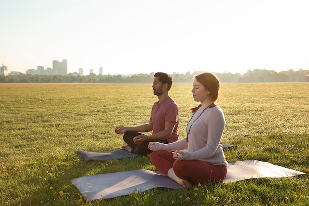 Vista lateral del hombre y la mujer meditando al aire libre sobre esteras de yoga
