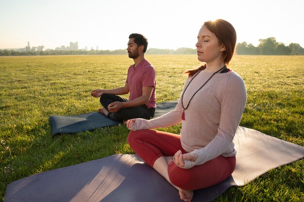 Vista lateral del hombre y la mujer meditando al aire libre sobre esteras de yoga