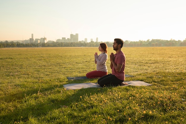 Foto gratuita vista lateral del hombre y la mujer meditando al aire libre sobre esteras de yoga