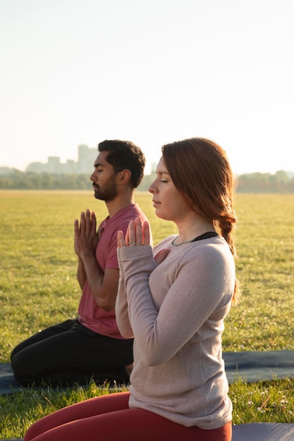 Vista lateral del hombre y la mujer meditando al aire libre sobre esteras de yoga