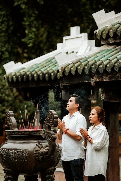 Vista lateral del hombre y la mujer rezando en el templo con incienso ardiente
