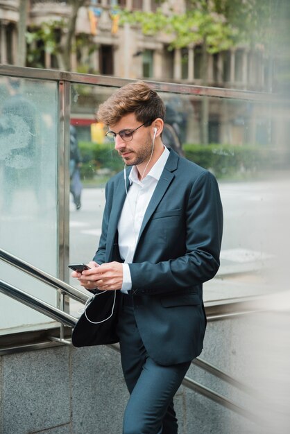 Vista lateral de un hombre de negocios usando un teléfono móvil con su auricular en las orejas