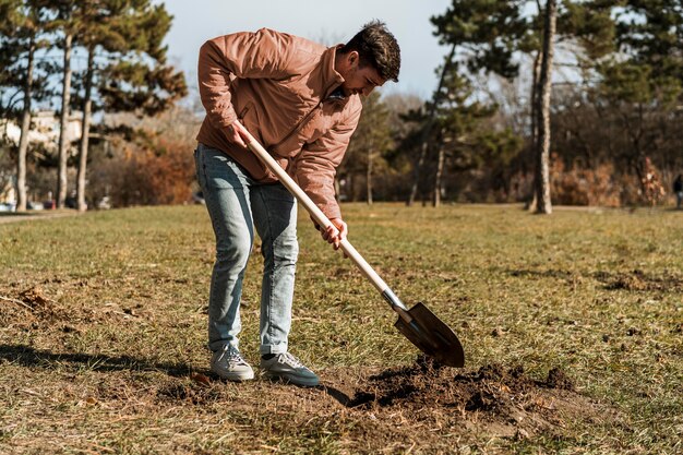 Vista lateral del hombre con pala para cavar un hoyo para plantar un árbol