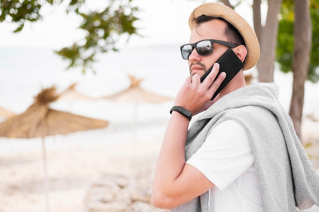 Vista lateral del hombre en la playa hablando por teléfono inteligente