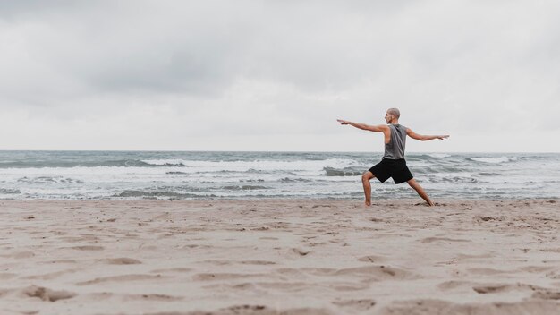 Vista lateral del hombre en la playa haciendo ejercicio de yoga con espacio de copia