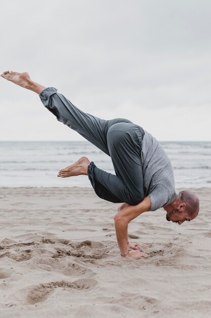 Vista lateral del hombre en la playa practicando posiciones de yoga