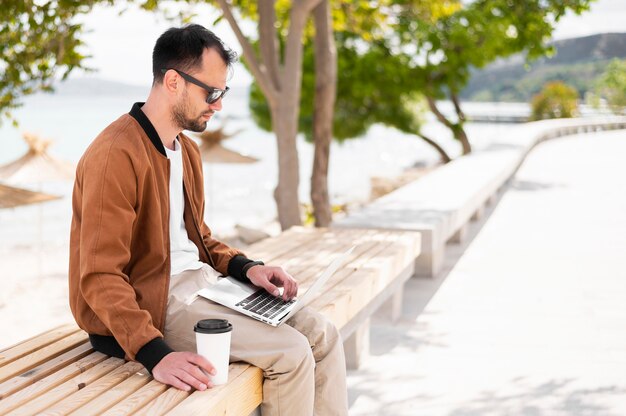 Vista lateral del hombre en la playa trabajando en la computadora portátil