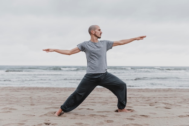 Vista lateral del hombre practicando posiciones de yoga al aire libre