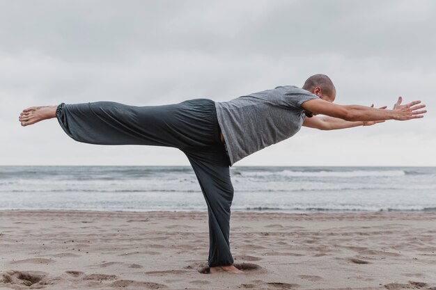 Vista lateral del hombre practicando yoga en la playa