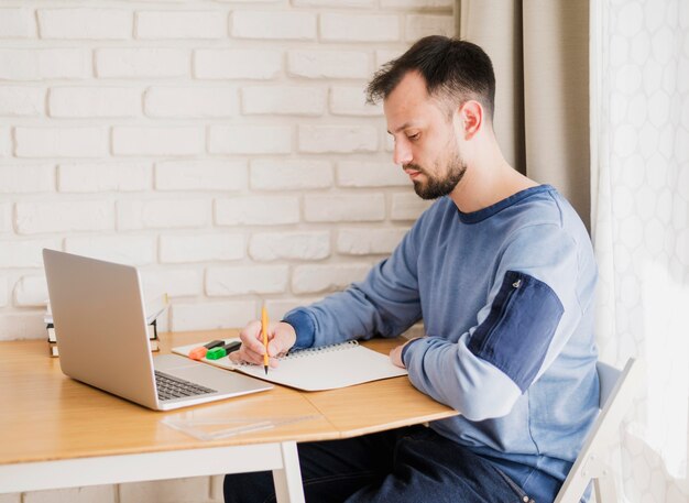 Vista lateral del hombre que aprende en línea desde la computadora portátil