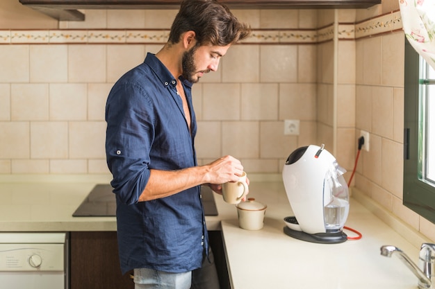 Vista lateral del hombre que se coloca en la cocina que sostiene la taza de café