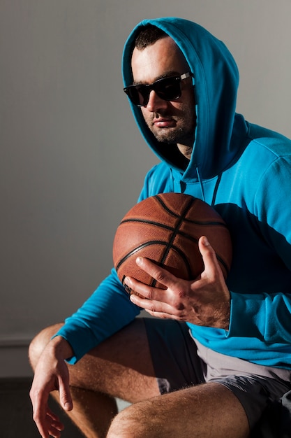 Foto gratuita vista lateral del hombre que llevaba una sudadera con capucha posando mientras sostiene baloncesto