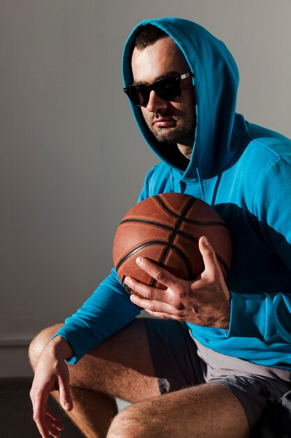 Vista lateral del hombre que llevaba una sudadera con capucha posando mientras sostiene baloncesto