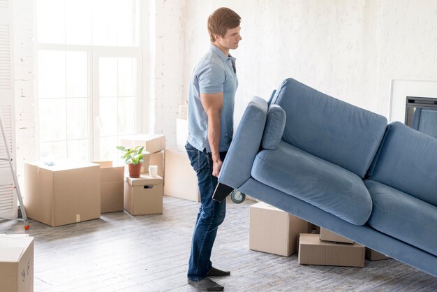 Vista lateral del hombre que maneja el sofá mientras se prepara para mudarse