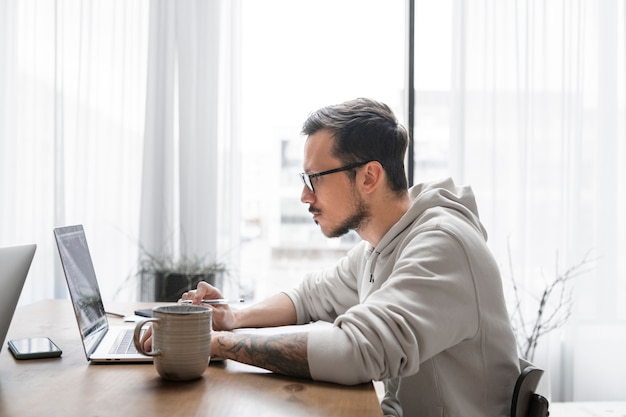 Vista lateral del hombre que trabaja en el escritorio desde casa con un portátil