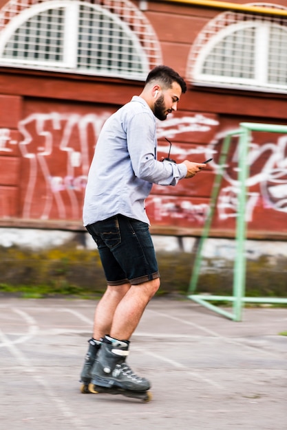 Vista lateral de un hombre que usa el teléfono móvil mientras que rollerskating en patín parque