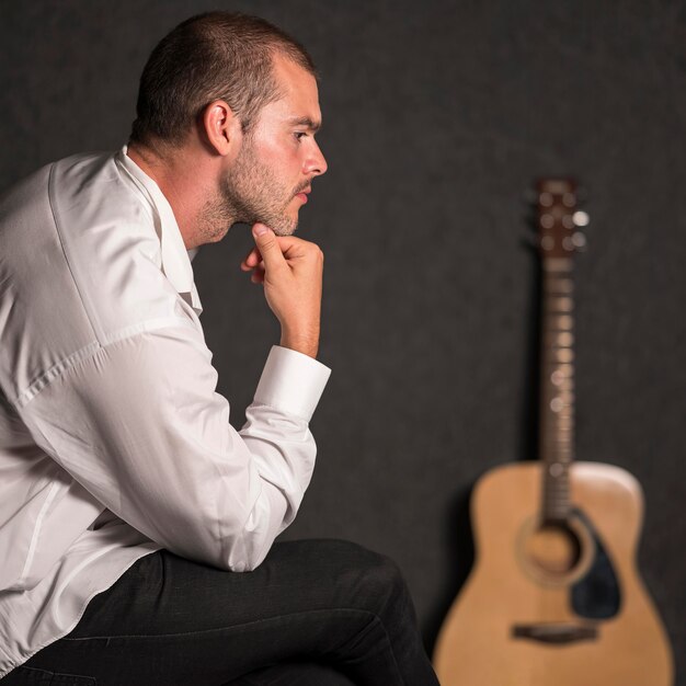 Vista lateral hombre sentado y guitarra acústica borrosa