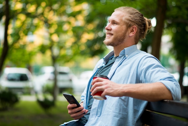 Vista lateral del hombre sonriente al aire libre con teléfono inteligente