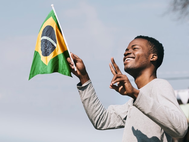 Vista lateral del hombre sonriente que sostiene la bandera brasileña