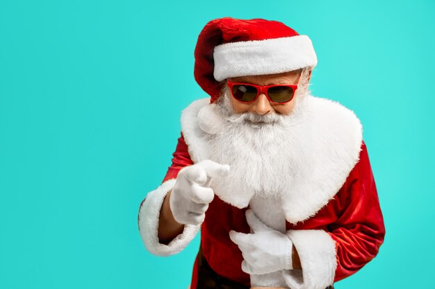 Vista lateral del hombre sonriente en traje rojo de Santa Claus. Retrato aislado del varón mayor con la barba blanca en gafas de sol. Concepto de vacaciones