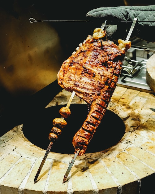 Vista lateral hombre sostiene carne de cordero frito en brochetas con papas fritas en un horno tandoor