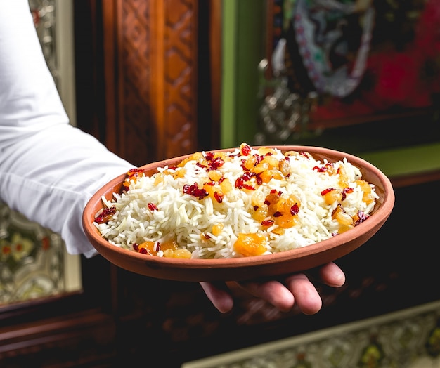 Vista lateral, un hombre sostiene un plato con arroz hervido con pasas y agracejos
