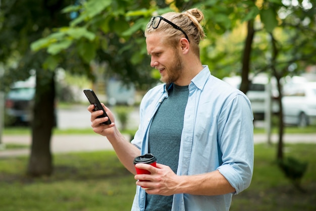 Vista lateral del hombre con teléfono y taza al aire libre