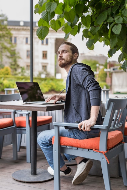 Vista lateral del hombre en una terraza de la ciudad con laptop