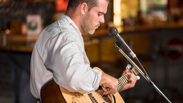 Vista lateral del hombre tocando la guitarra en un bar.