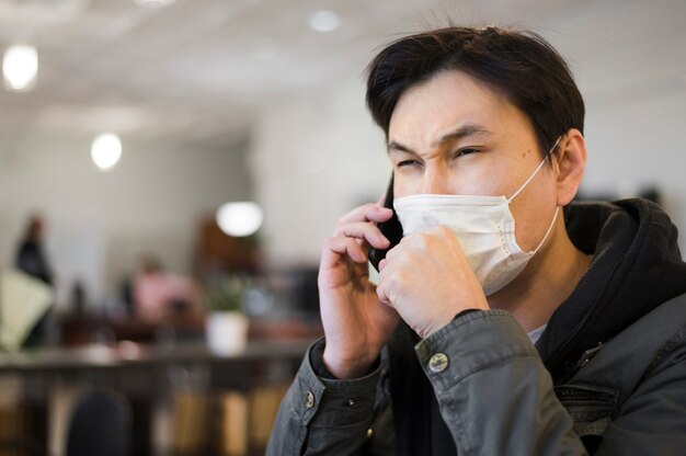 Vista lateral del hombre tosiendo en máscara médica mientras habla por teléfono