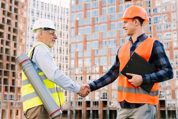 Vista lateral hombres con chalecos de seguridad dándose la mano