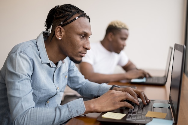 Vista lateral de hombres trabajando en computadoras portátiles en la oficina